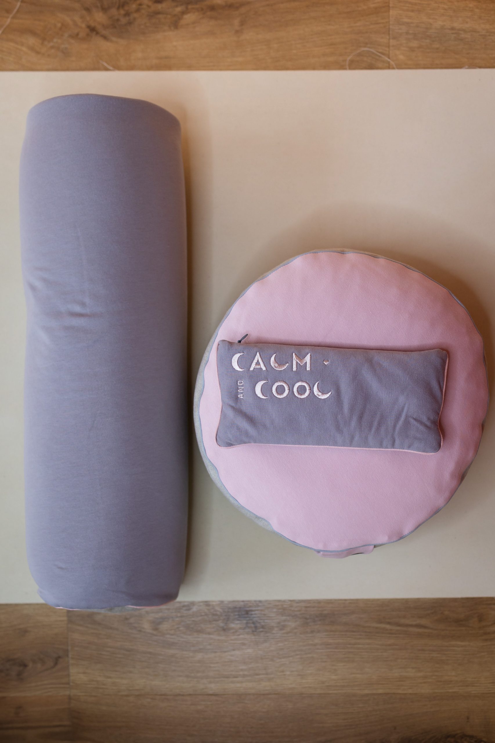 Pink and gray yoga bolster and cushion on wooden floor.