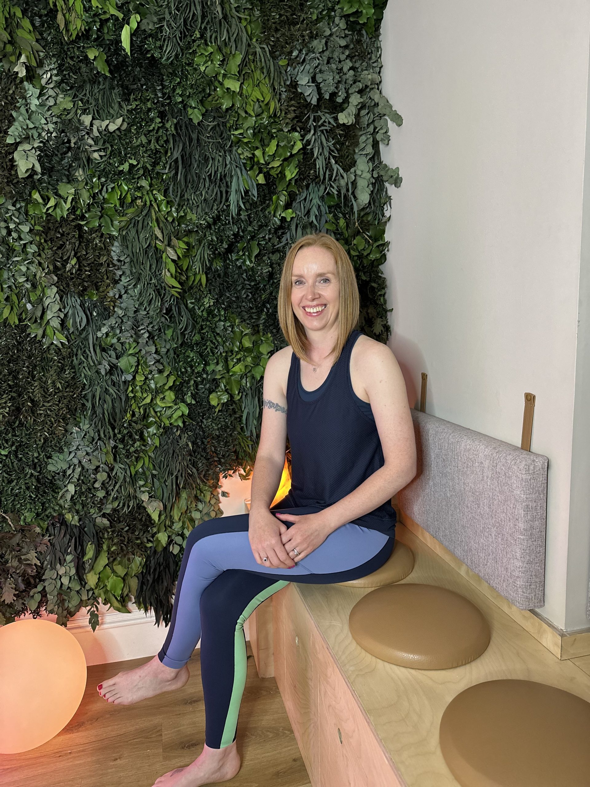 Woman smiling seated against indoor green plant wall